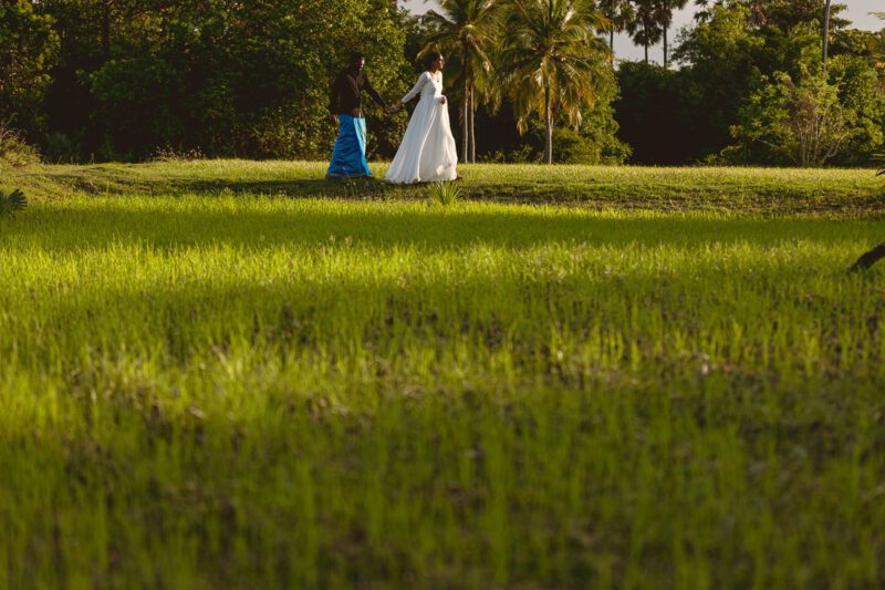 Bride and groom Kobe and Ramya walking hand in hand at Jaffna Fort, with the historic stone walls and ocean backdrop. Romantic post-wedding shoot by Banu Photography.
