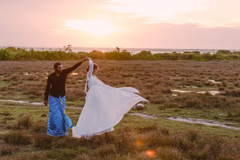 Bride and groom Kobe and Ramya walking hand in hand at Jaffna Fort, with the historic stone walls and ocean backdrop. Romantic post-wedding shoot by Banu Photography.