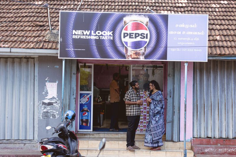 Kobe and Ramya walking through the quiet streets of Jaffna city, surrounded by colonial-style buildings and everyday life. A candid post-wedding moment captured by Banu Photography
