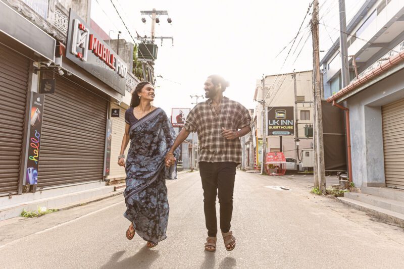 Kobe and Ramya walking through the quiet streets of Jaffna city, surrounded by colonial-style buildings and everyday life. A candid post-wedding moment captured by Banu Photography