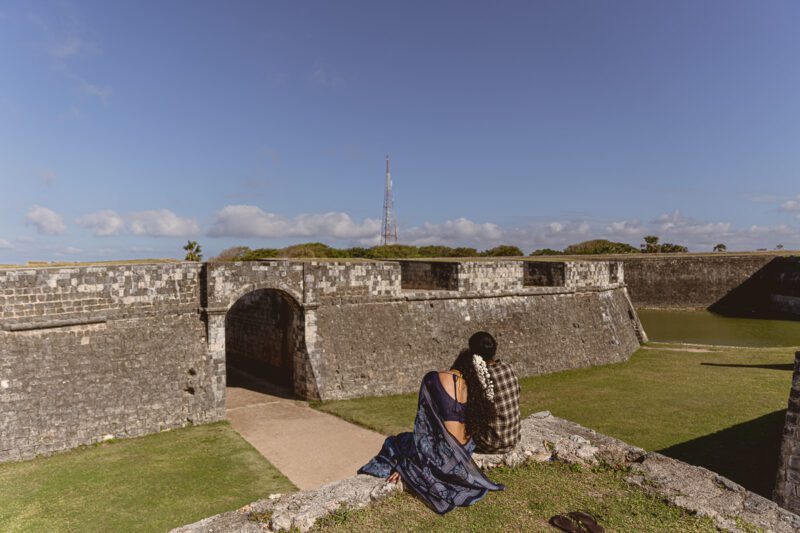 Bride and groom Kobe and Ramya walking hand in hand at Jaffna Fort, with the historic stone walls and ocean backdrop. Romantic post-wedding shoot by Banu Photography.