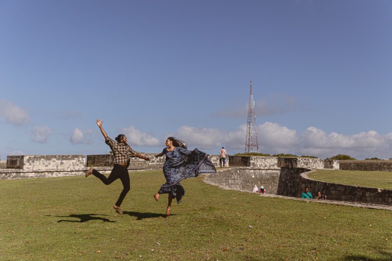 Bride and groom Kobe and Ramya walking hand in hand at Jaffna Fort, with the historic stone walls and ocean backdrop. Romantic post-wedding shoot by Banu Photography.